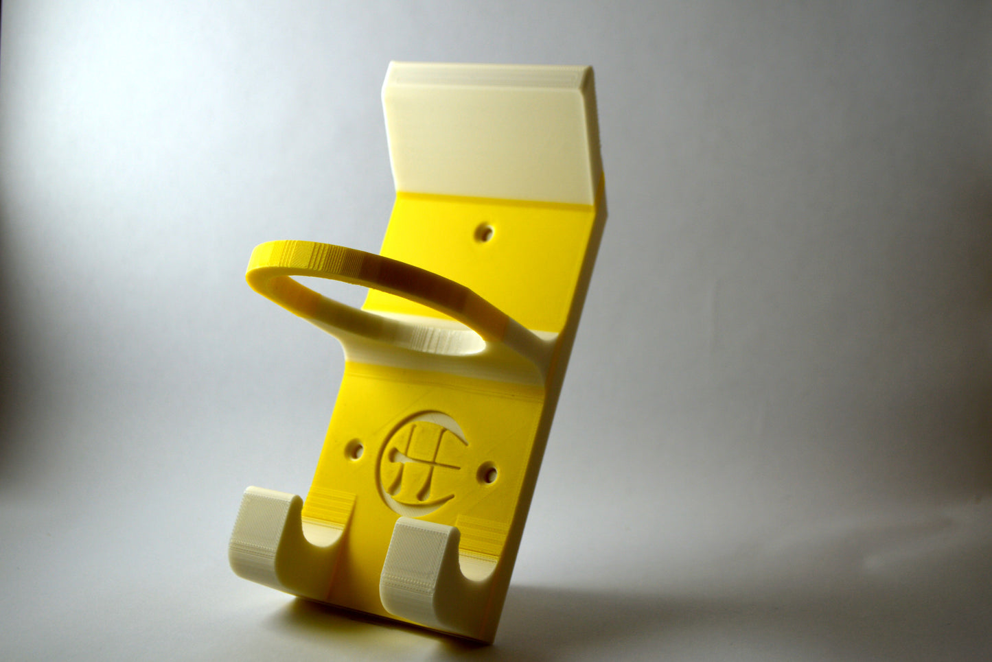 A white and yellow hurling holder with a logo cut into the design, featuring a helmet hook and a hurley hook and a sliotar holder.