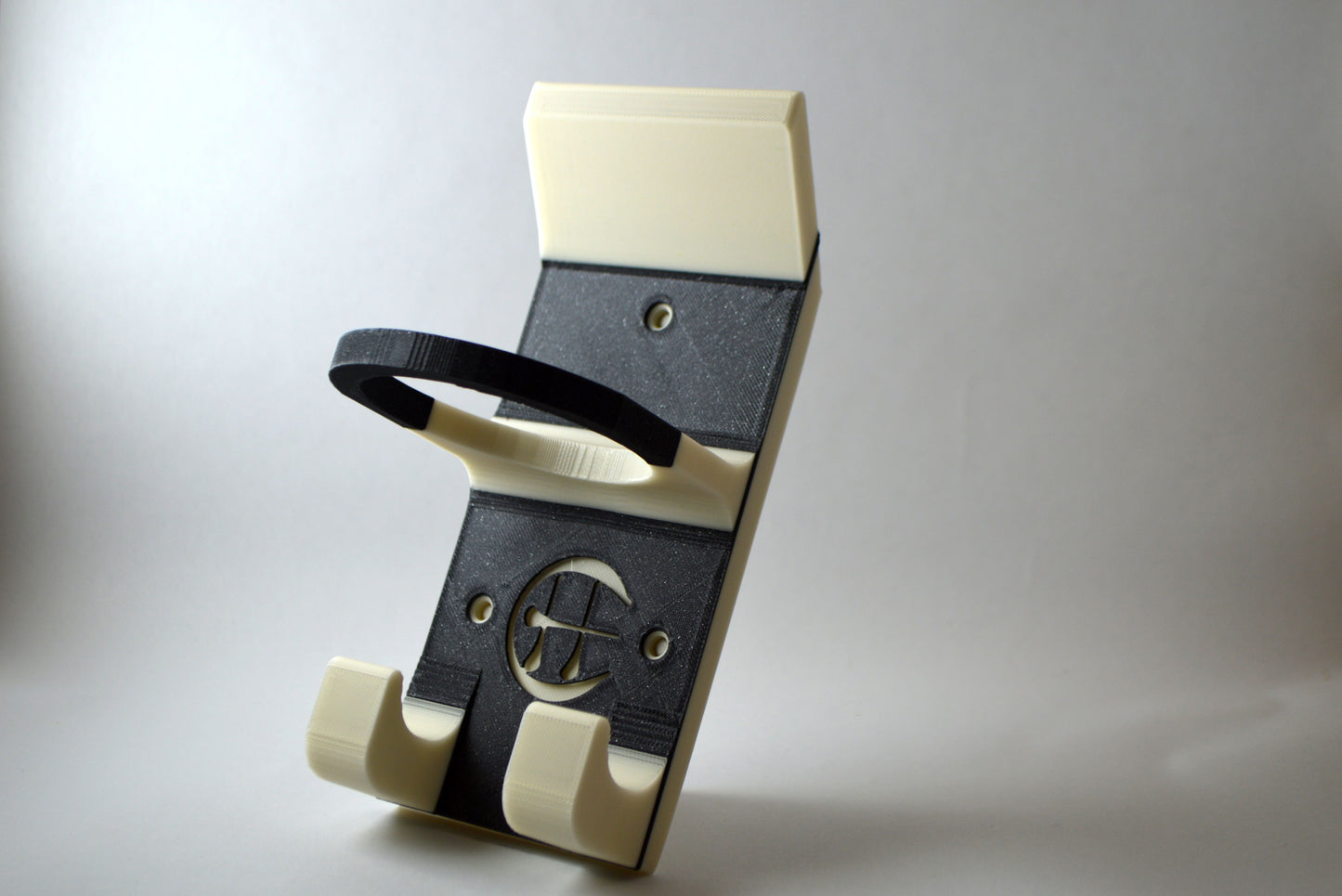 A black and white hurling holder with a logo cut into the design, featuring a helmet hook and a hurley hook and a sliotar holder, placed against a grey background.