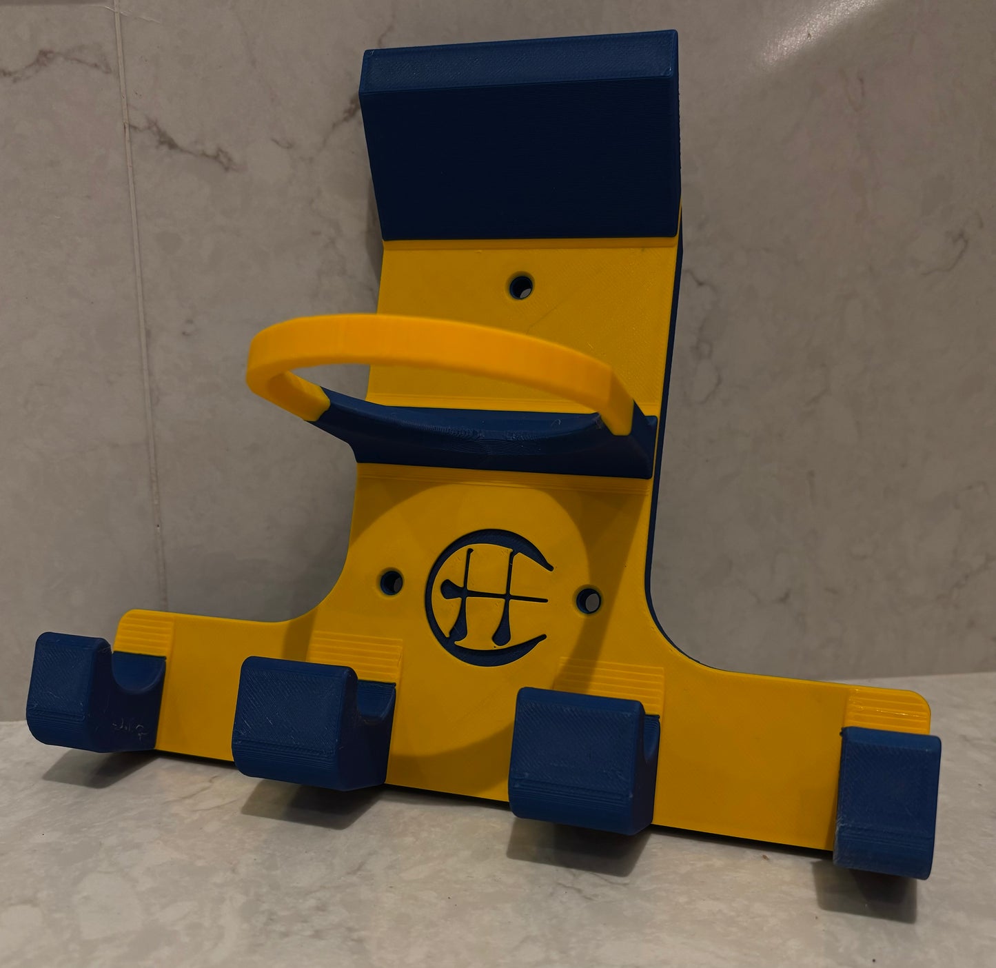 A blue and yellow triple trinity hurley holder designed to hold equipment for the sport of hurling, featuring hooks for a helmet, sliotar, and multiple hurleys.