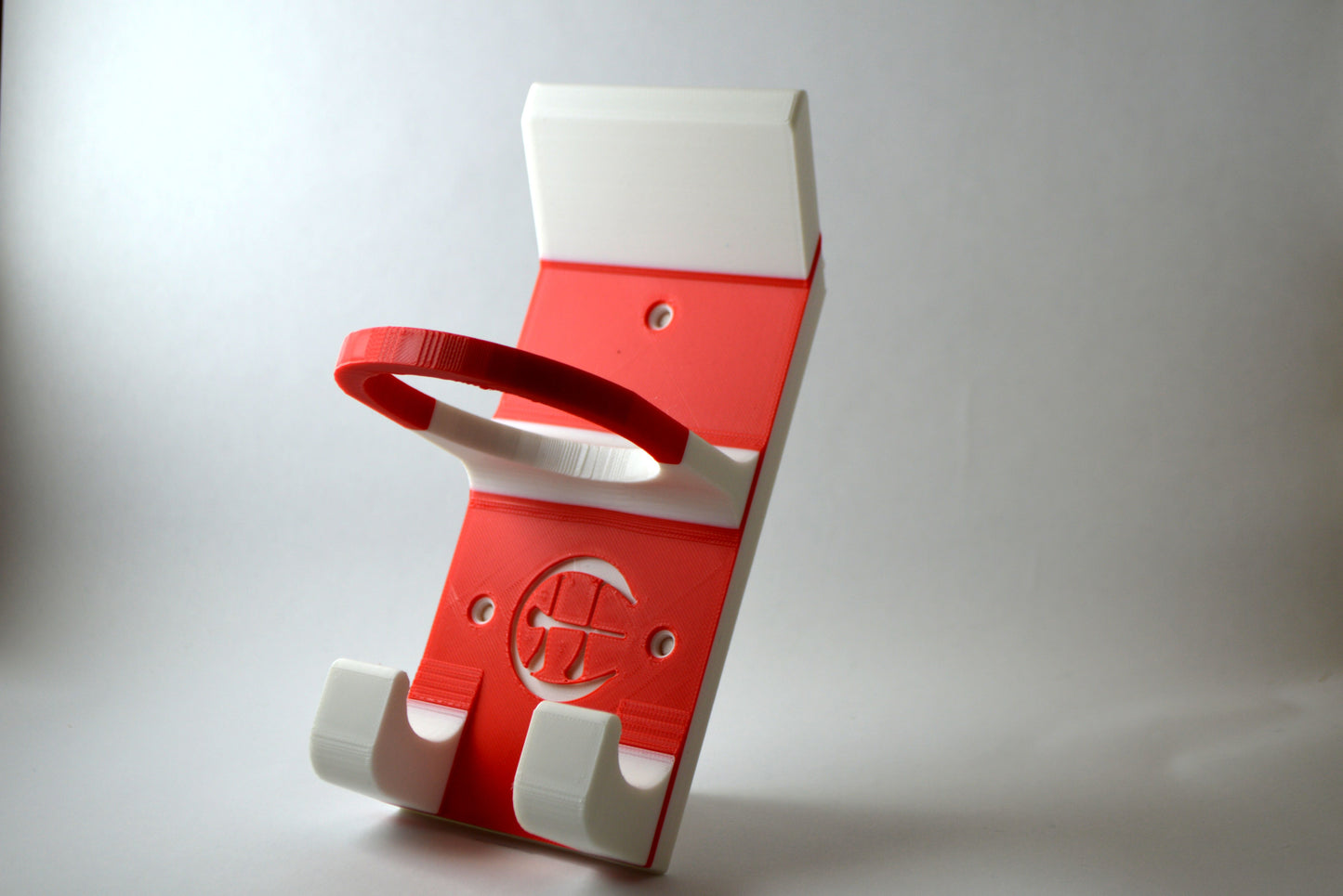 A red and white hurling holder with a logo cut into the design, featuring a helmet hook and a hurley hook and a sliotar holder.