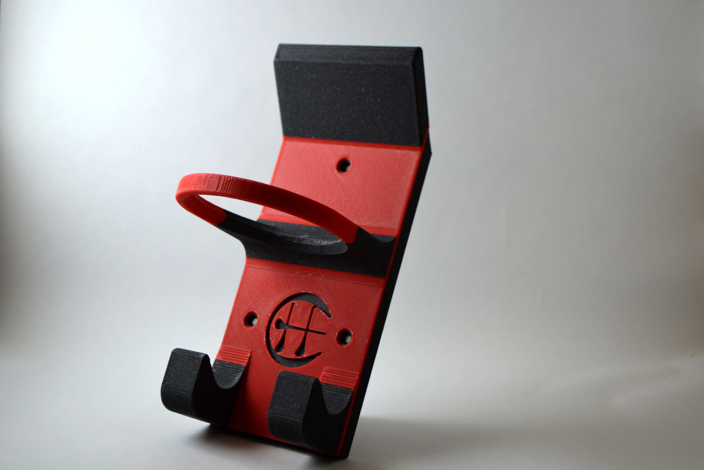A red and black hurling holder with a logo cut into the design, featuring a helmet hook and a hurley hook and a sliotar holder.