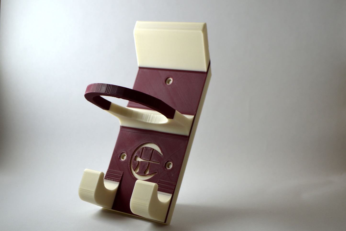 A maroon and white hurling holder with a logo cut into the design, featuring a helmet hook and a hurley hook and a sliotar holder.