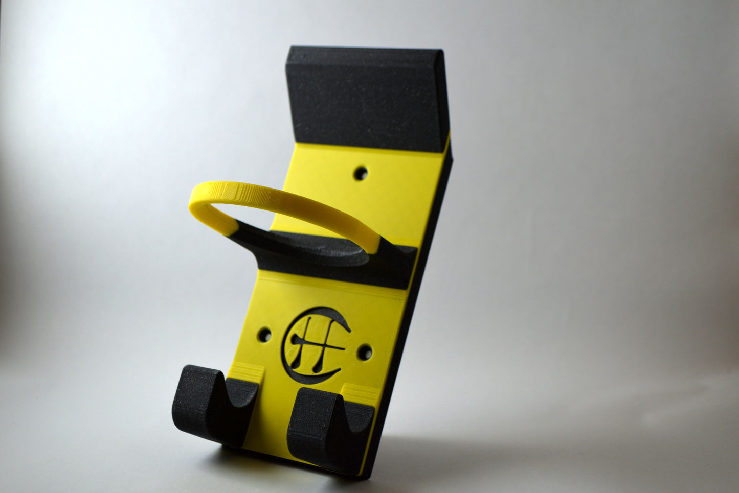 A black and amber hurling holder with a logo cut into the design, featuring a helmet hook and a hurley hook and a sliotar holder.
