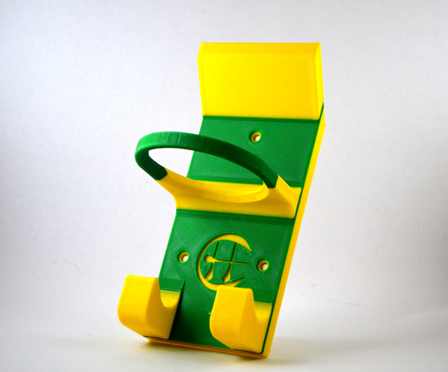 A green and yellow hurling holder with a logo cut into the design, featuring a helmet hook and a hurley hook and a sliotar holder, placed against a grey background.