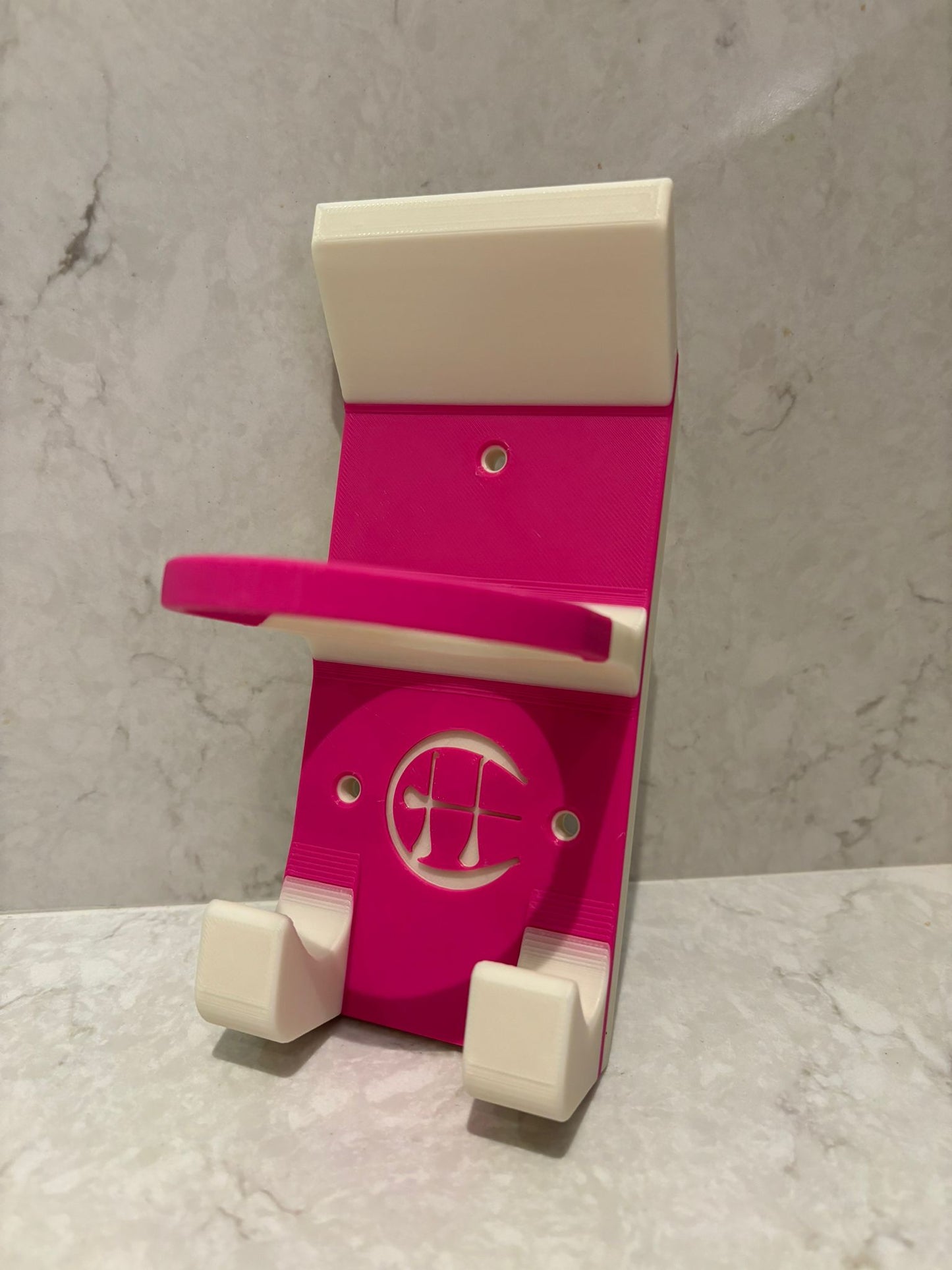 A pink and white hurling holder with a logo cut into the design, featuring a helmet hook and a hurley hook and a sliotar holder.