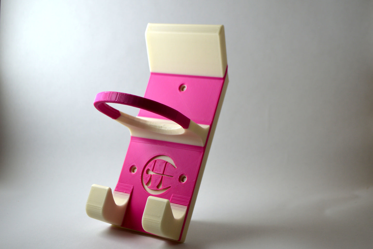A pink and white hurling holder with a logo cut into the design, featuring a helmet hook and a hurley hook and a sliotar holder.