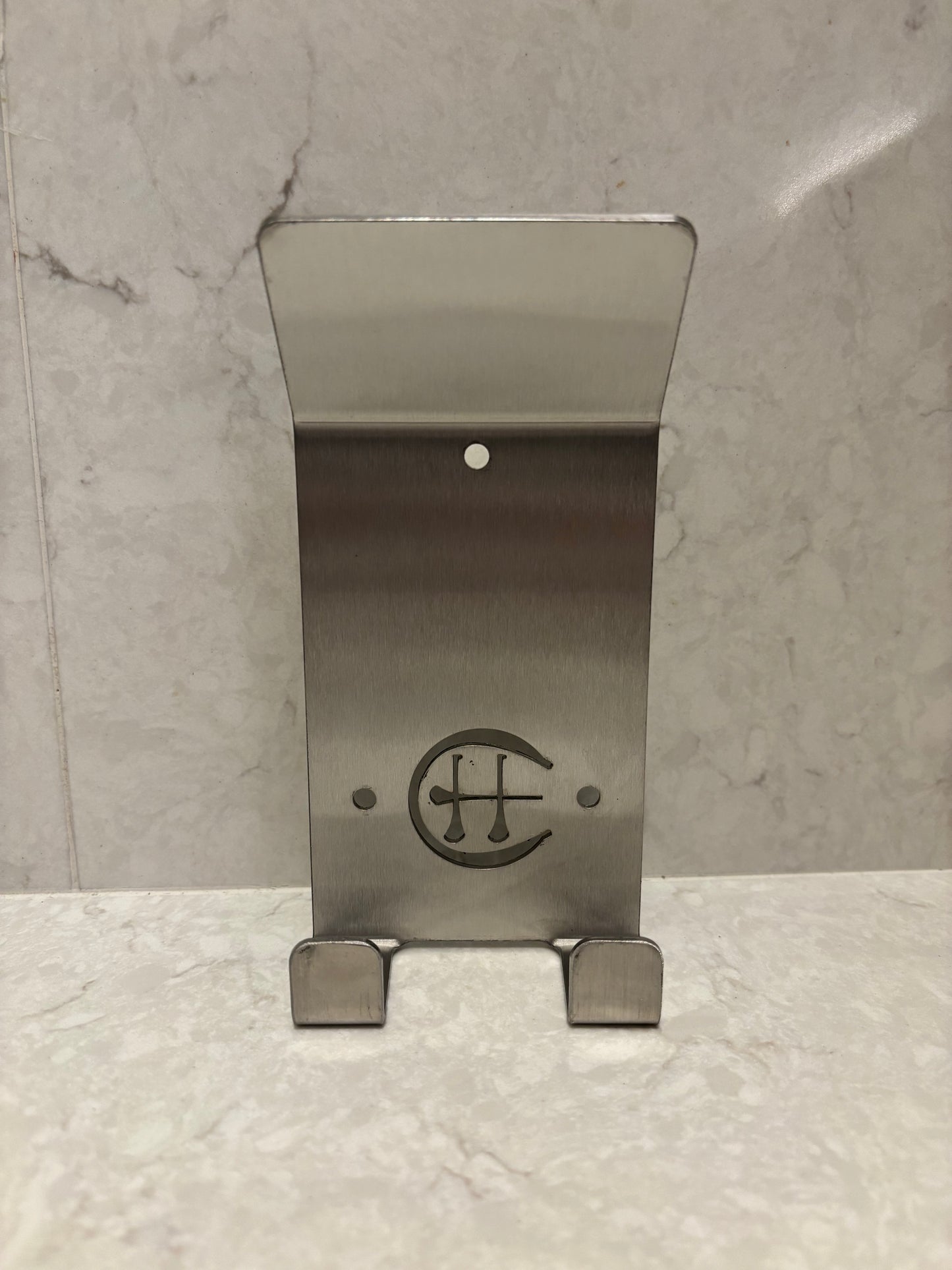 A stainless steel Dual Star hurling holder with a logo cut into the design, featuring a helmet hook and a hurley hook, placed against a grey background.