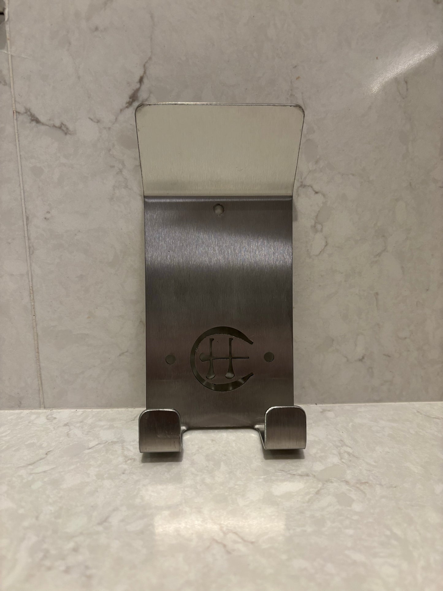 A stainless steel Dual Star hurling holder with a logo cut into the design, featuring a helmet hook and a hurley hook, placed against a grey background.
