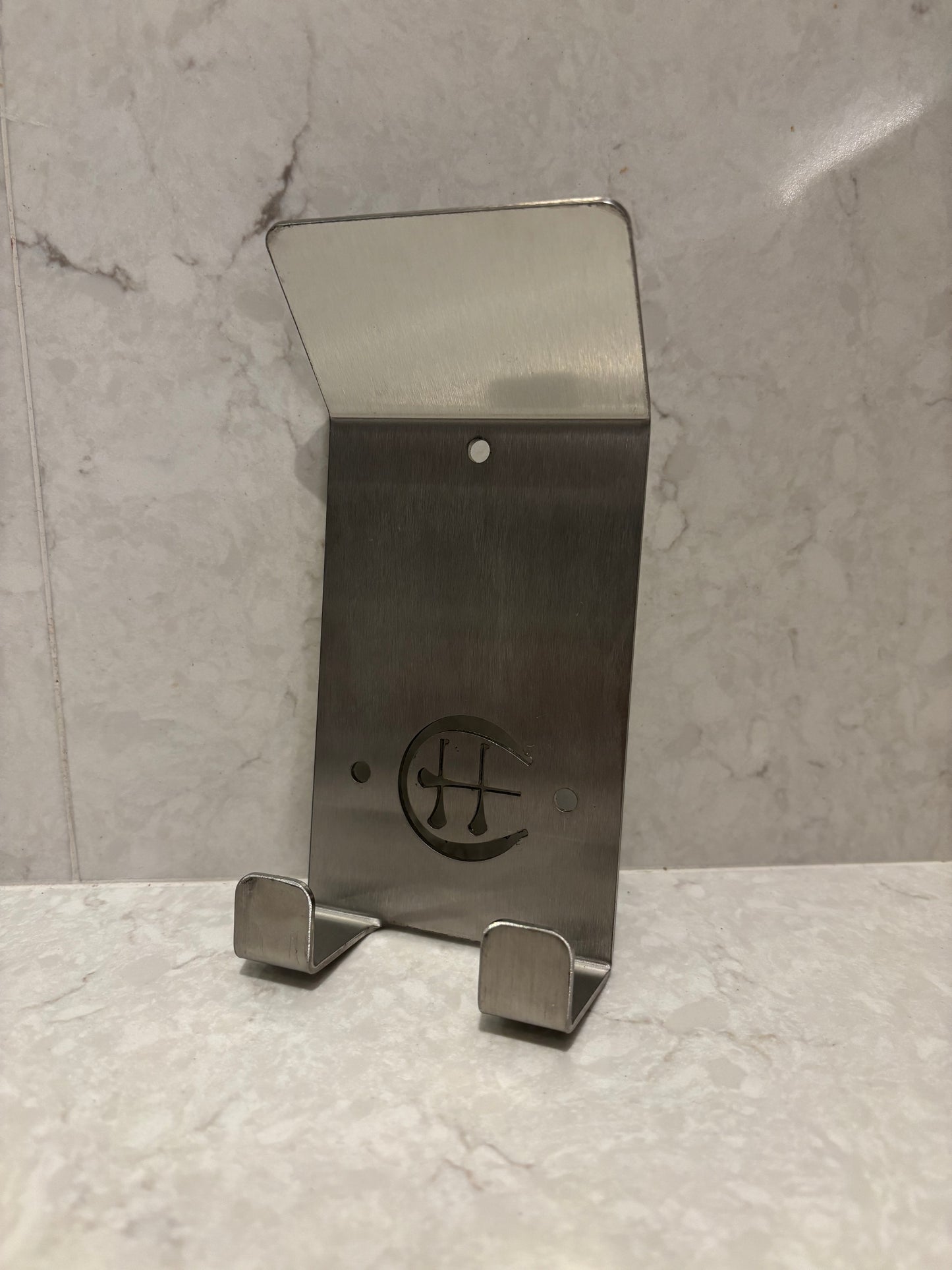 A stainless steel Dual Star hurling holder with a logo cut into the design, featuring a helmet hook and a hurley hook, placed against a grey background.