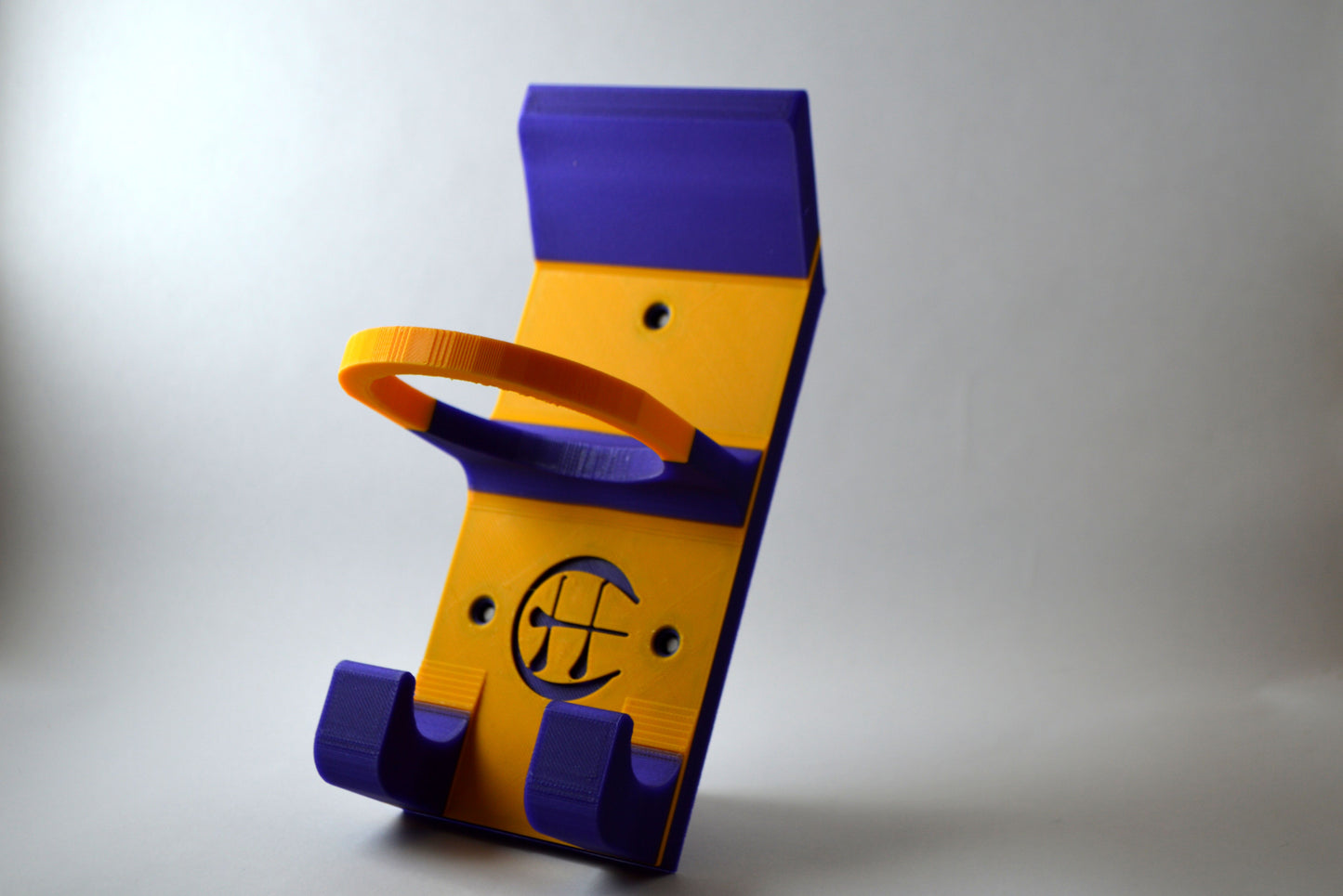 A yellow and purple hurling holder with a logo cut into the design, featuring a helmet hook and a hurley hook and a sliotar holder.
