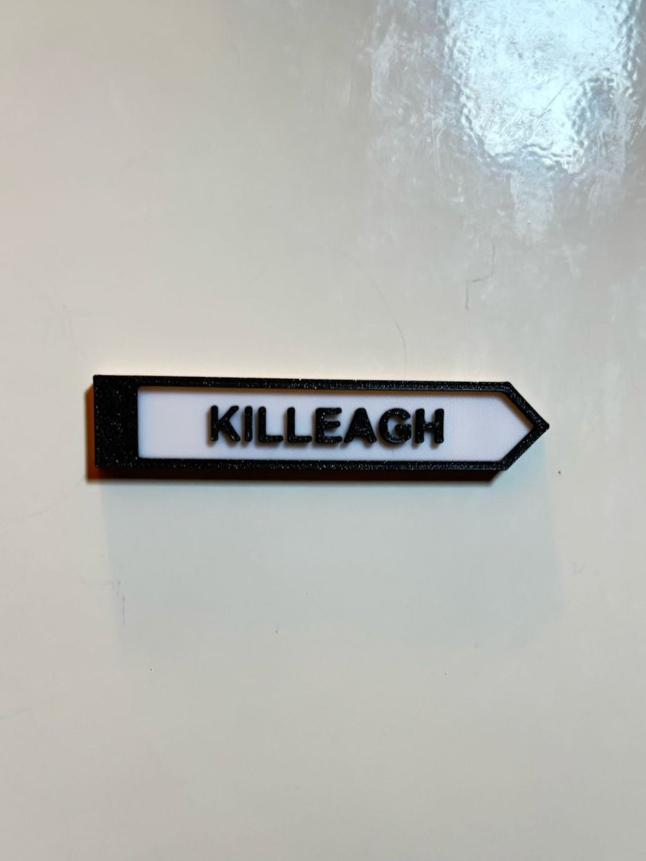 A black and white rectangular fridge magnet with white text 'Cill La KILLEAGH' on a white wall, representing a miniature size signpost.
