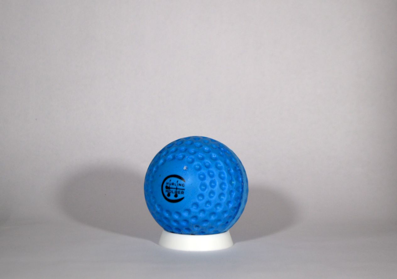 A blue textured fireball / speedball with a black circular logo, displayed on a small white stand against a neutral gray background.