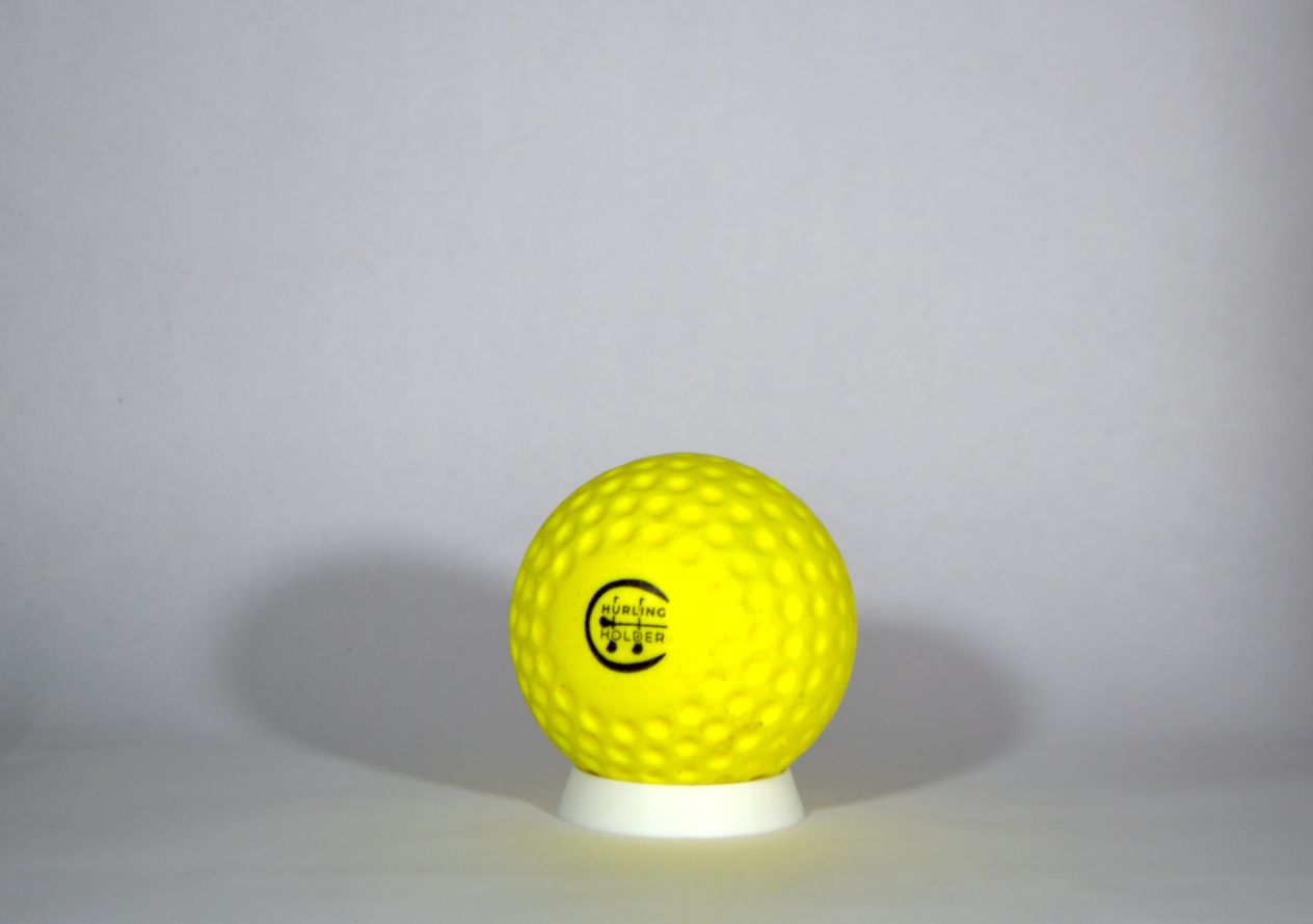 A bright yellow fireball / speedball with a black circular logo, displayed on a small white pedestal against a neutral gray background.
