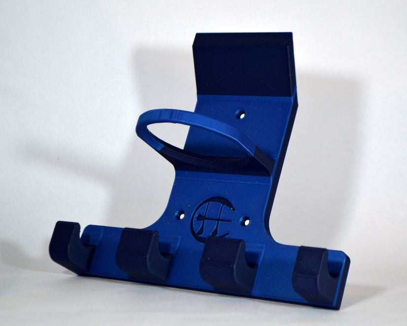A blue and navy plastic wall-mounted hurling and camogie holder stand with four hooks on the bottom, photographed against a plain light grey wall and floor.
