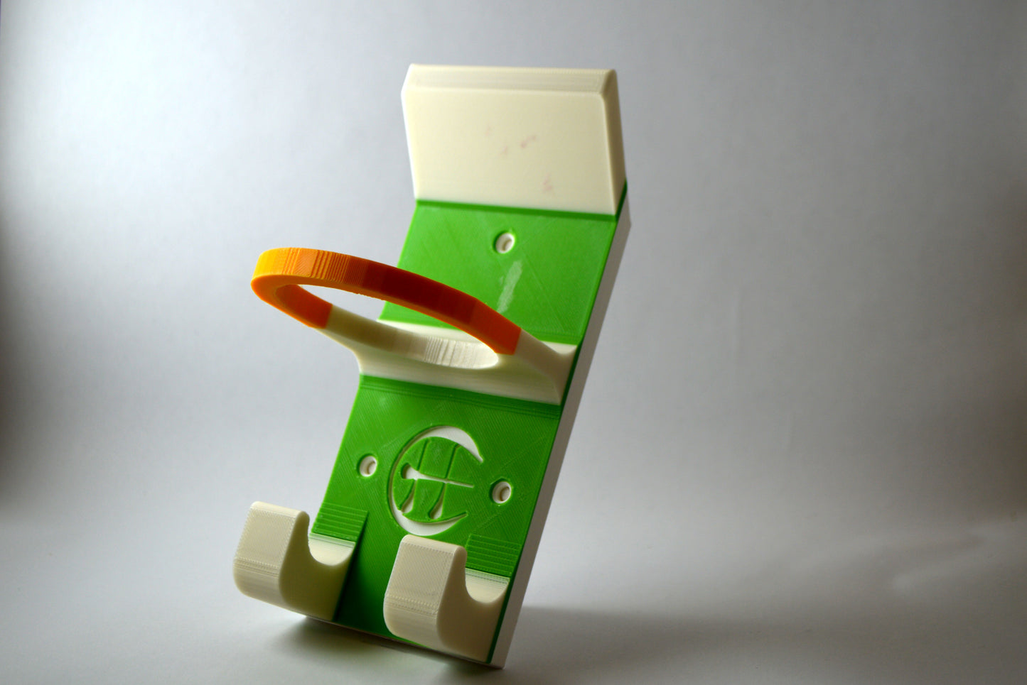 A white and yellow and green hurling holder with a logo cut into the design, featuring a helmet hook and a hurley hook and a sliotar holder.
