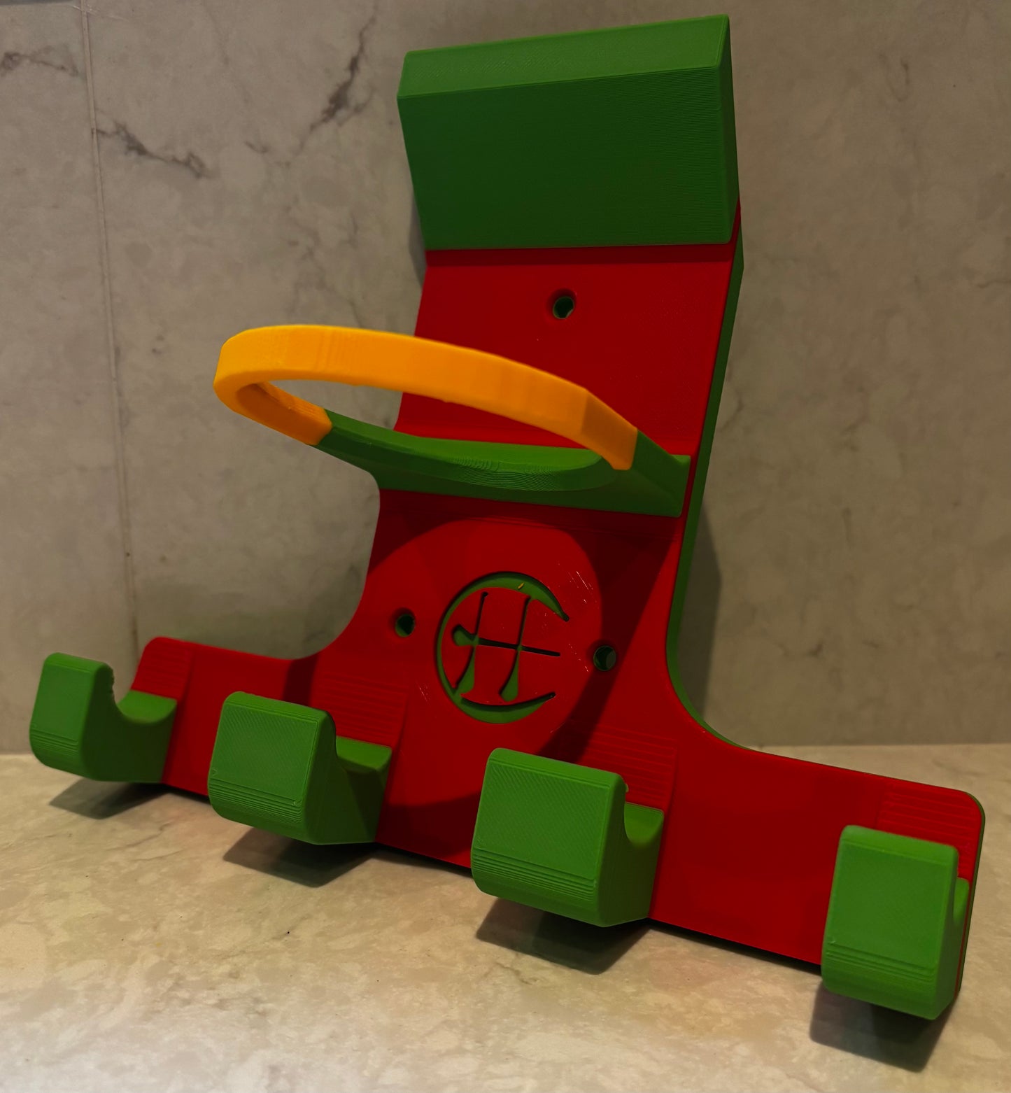 A red and green and yellow triple hurling holder with a logo cut into the design, featuring a helmet hook and a hurley hook and a sliotar holder.