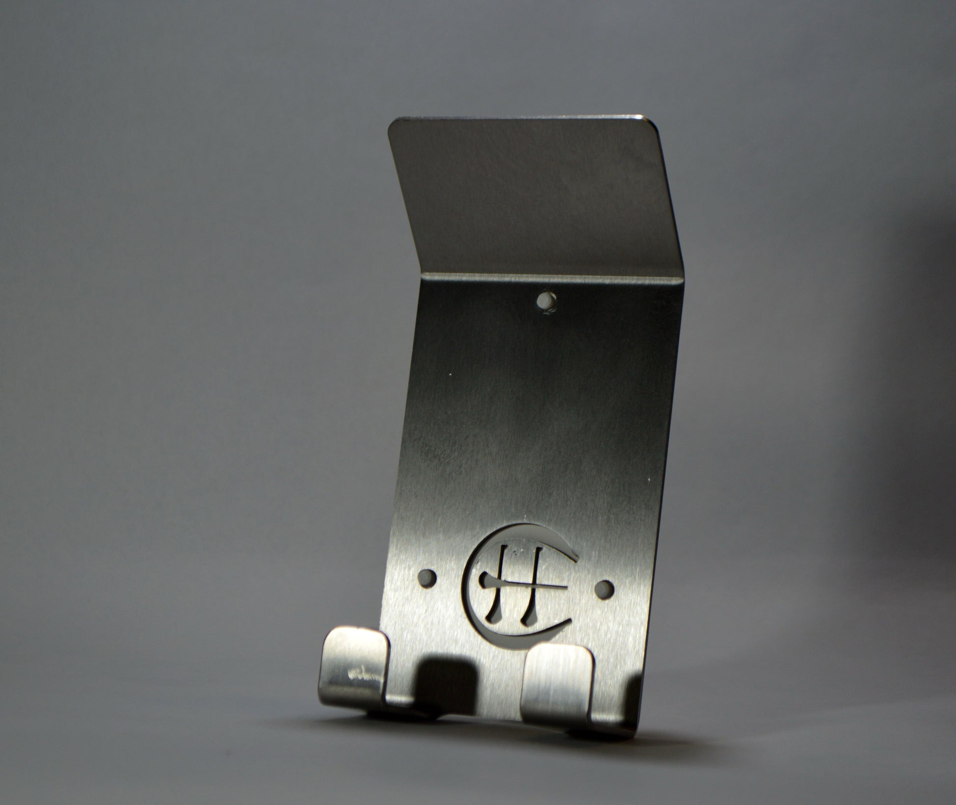 A stainless steel Dual Star hurling holder with a logo cut into the design, featuring a helmet hook and a hurley hook, placed against a grey background.