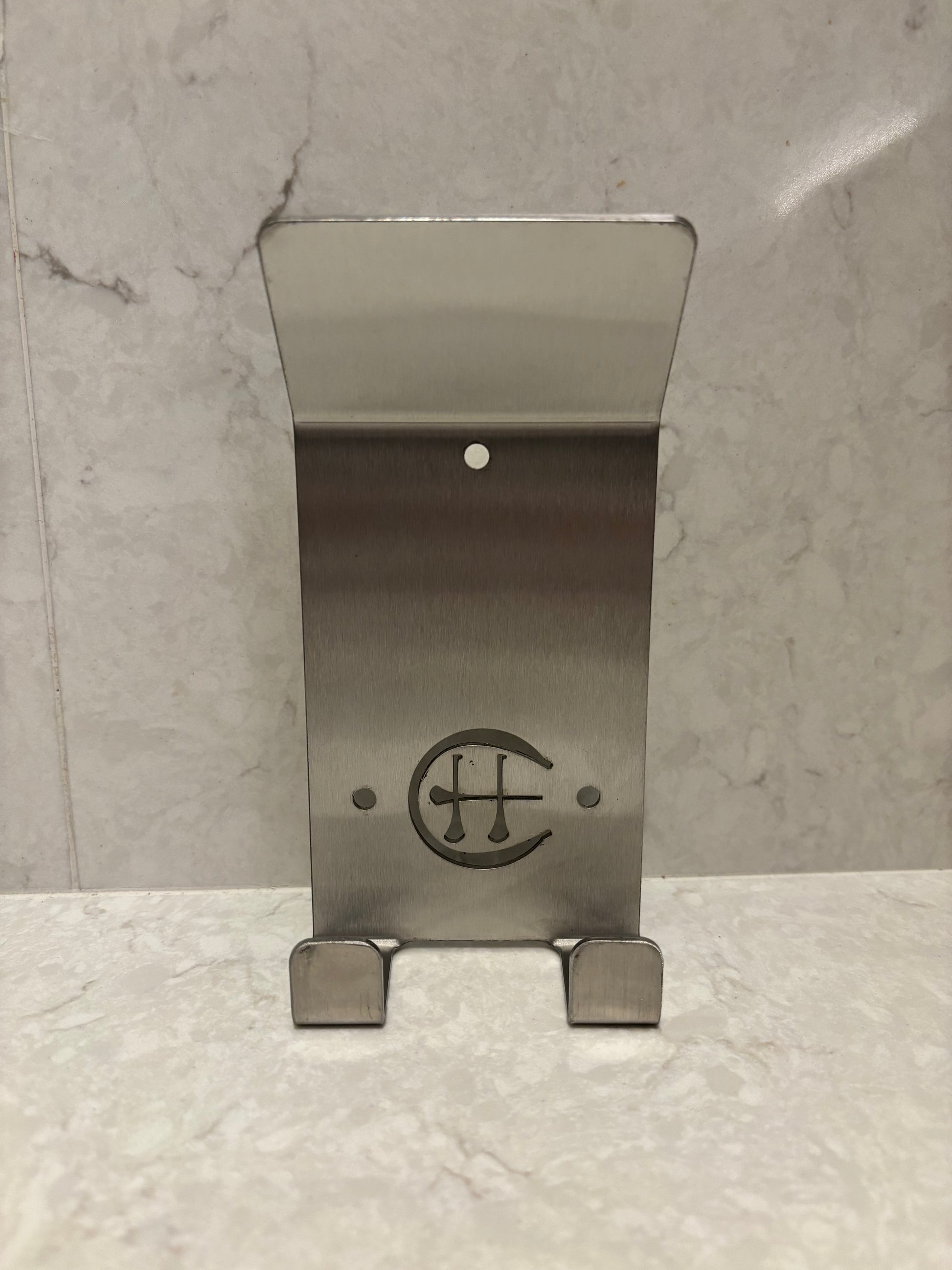 A stainless steel Dual Star hurling holder with a logo cut into the design, featuring a helmet hook and a hurley hook, placed against a grey background.