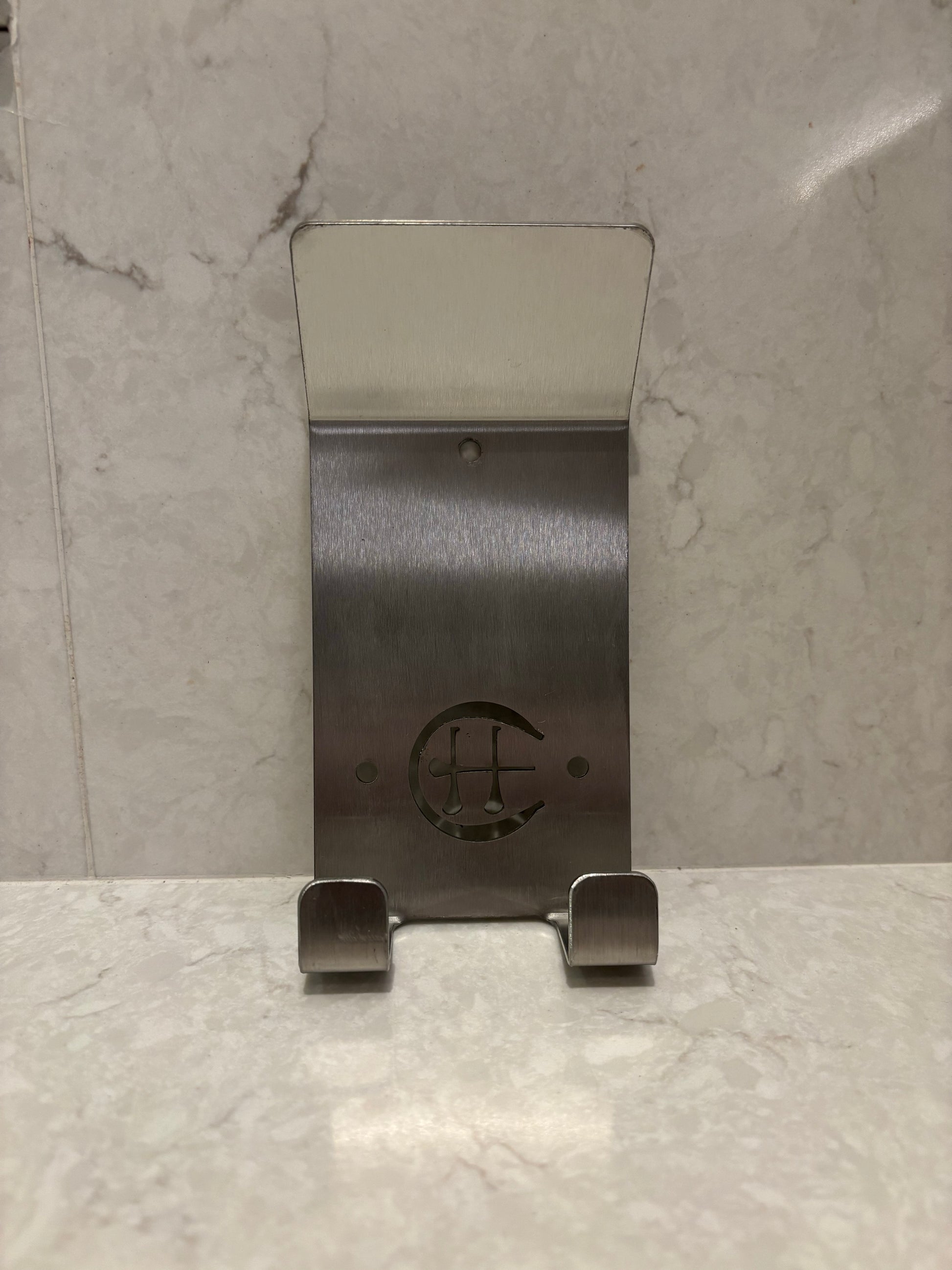 A stainless steel Dual Star hurling holder with a logo cut into the design, featuring a helmet hook and a hurley hook, placed against a grey background.