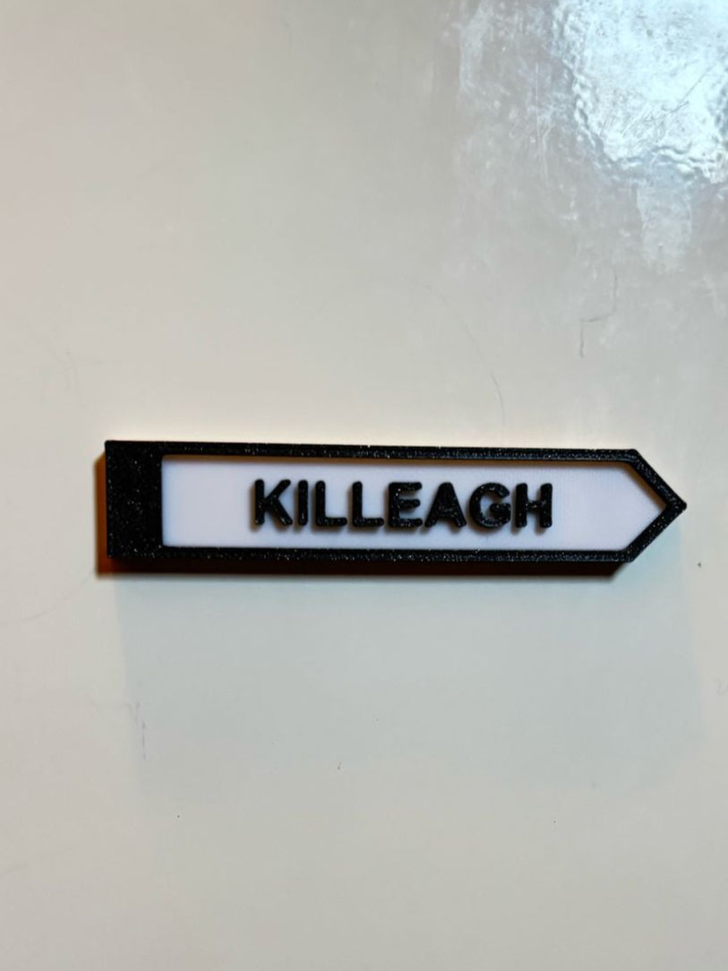 A black and white rectangular fridge magnet with white text 'Cill La KILLEAGH' on a white wall, representing a miniature size signpost.
