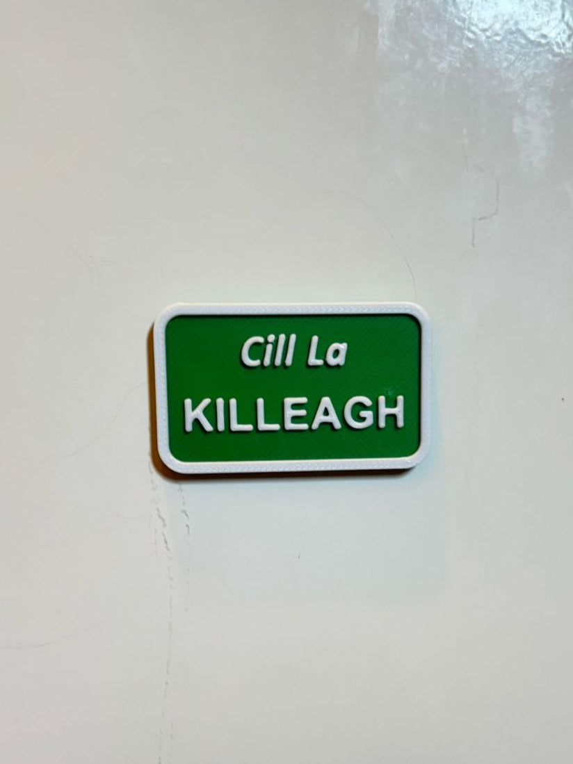 A green rectangular fridge magnet with white text 'Cill La KILLEAGH' on a white wall, representing a miniature size signpost.