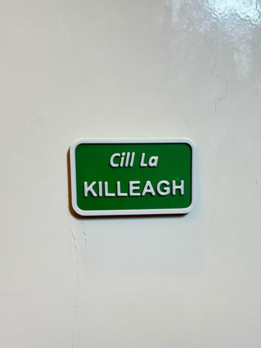 A green rectangular fridge magnet with white text 'Cill La KILLEAGH' on a white wall, representing a miniature size signpost.